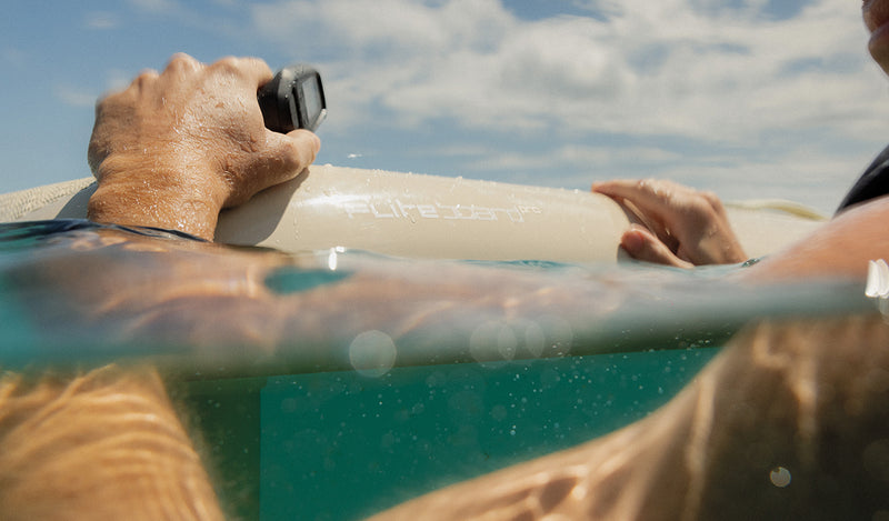 Fliteboard Pro: Person holding eFoil remote in clear water under blue sky.