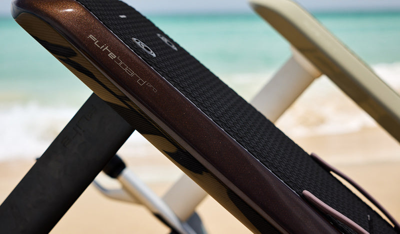 Fliteboard Pro, e-foil board resting on a beach with turquoise ocean.