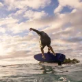 A person riding a Ultramarine Fliteboard Ultra L3 eFoil above ocean waves at sunset.